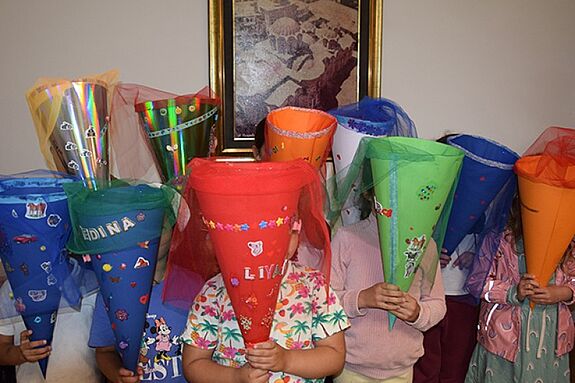 Mehrere Kinder halten selbstgebastelte, bunt verzierte Schultüten mit Tüll vor sich in einem Innenraum.