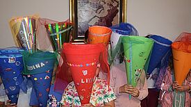 Mehrere Kinder halten selbstgebastelte, bunt verzierte Schultüten mit Tüll vor sich in einem Innenraum.