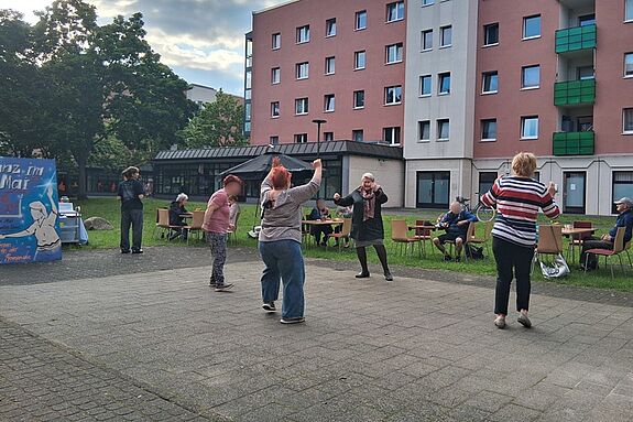 Mehrere Frauen bewegen sich tanzend vor einem Haus. 