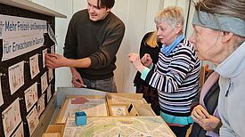 Teilnehmende stehen an einem Tisch, auf dem eine Karte des Quartiers liegt. Verschiedene Flächen für mögliche Sportangebote werden auf der Karte mit Pinnadeln markiert.  