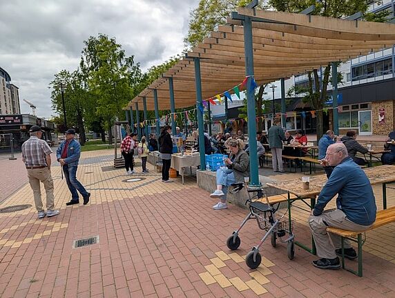 Menschen sitzen und stehen bei einem Nachbarschaftsfest auf dem Quartiersplatz im Kosmosviertel.