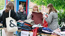 Vier Personen stehen beim Saisonauftakt auf dem Letteplatz am Kleidertauschtisch.