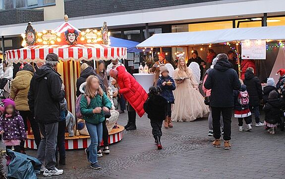 Personen bewegen sich auf Wintermarkt im QM-Gebiet Thermometersiedlung vor einem Karussell und einem Stand. 