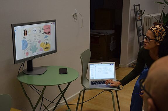 Eine Person präsentiert einen Flyer-Entwurf auf einem Laptop und einem Monitor während der Quartiersratssitzung.