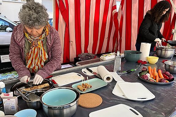 Zwei Projektmitglieder bereiten am Stand auf dem Kranoldplatz gefüllte Pfannkuchen für den Ernährungstag vor.