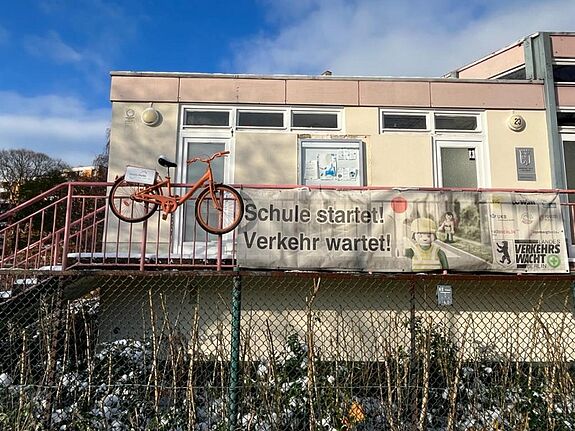 Ein orangefarbenes Fahrrad hängt am Geländer der Jugendverkehrsschule Gottschedstraße.