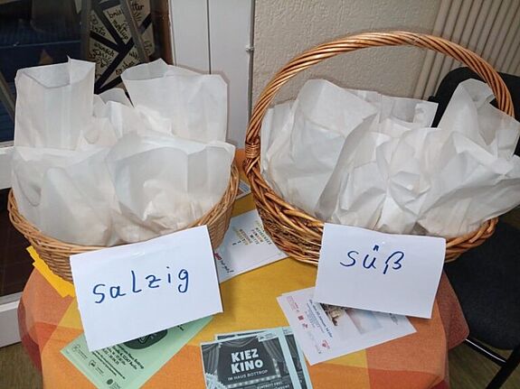 Zwei Körbe mit Popcorn-Tüten, beschriftet mit „salzig“ und „süß“, stehen auf einem Tisch.