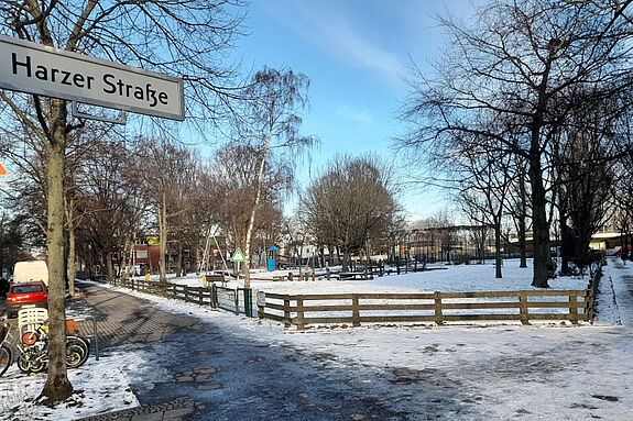 Blick auf einen verschneiten Spielplatz. Im Vordergrund ein Straßenschild mit der Aufschrift „Harzer Straße“.