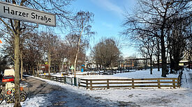 Blick auf einen verschneiten Spielplatz. Im Vordergrund ein Straßenschild mit der Aufschrift „Harzer Straße“.