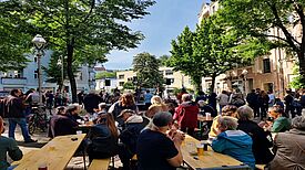 Beim Kiezfest im QM-Gebiet Flughafenstraße sitzen Personen an Tischen oder stehen vor der Bühne.