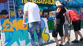 Jugendliche Worlshopteilnehmer sprühen ein Graffitti.