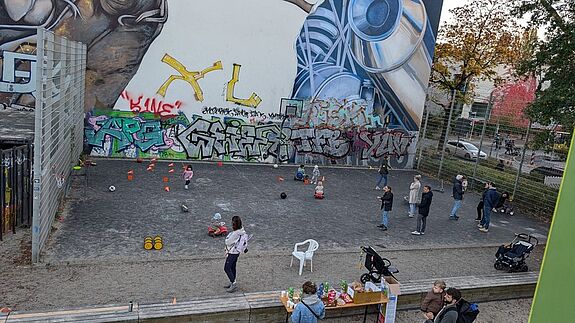 Familien und Kinder spielen und unterhalten sich auf dem Klara-Franke-Spielplatz, der von Graffiti-Kunst umgeben ist.