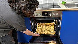 Eine Person schiebt ein Backblech in den Ofen, auf dem Nuggets liegen. 