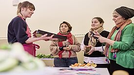 Ein Mitglied von RESTLOS GLÜCKLICH e. V. zeigt drei Frauen die Zubereitung eines Gerichts, das sie bei dem Workshop kennenlernen. 