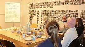 Fünf Teilnehmende sitzen um einen gedeckten Tisch und diskutieren. 