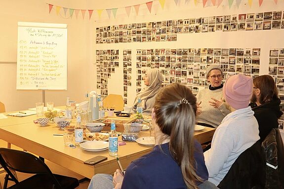 Fünf Teilnehmende sitzen um einen gedeckten Tisch und diskutieren. 