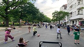 Kinder spielen auf einer temporär gesperrten Straße im Quartier Pankstraße, während Erwachsene die lebendige Atmosphäre genießen.