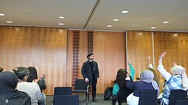 Der Abgeordnete Hakan Demir steht vor einer Gruppe von Menschen, die ihre Hände heben, um Fragen zu stellen.