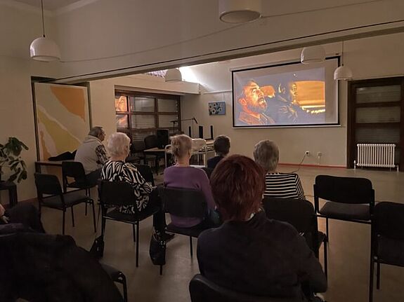 Menschen sitzen in einem abgedunkelten Raum und schauen sich den Film „Ziemlich beste Freunde“ auf einer Leinwand an.