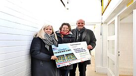 Von links nach rechts Ute Jansen von Outlaw gGmbH, Stadträtin Korinna Stephan und Staatssekretär Stephan Machulik halten einen symbolischen Schecks für die Kitasanierung.