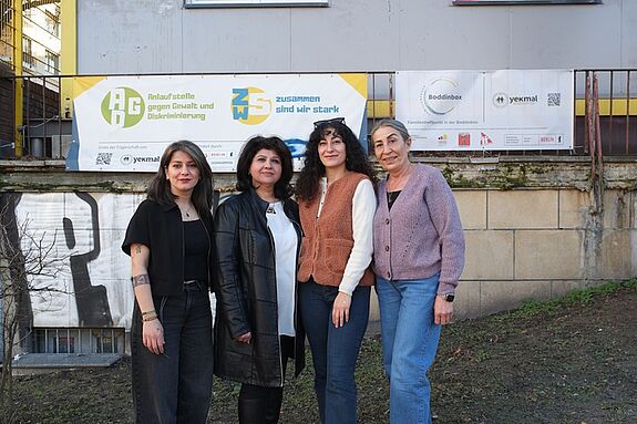 Vier Frauen posieren vor einem Gebäude und lächeln in die Kamera.