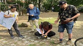 Vier Personen untersuchen im Freien mit Messgerät und Stadtplan die Temperatur am Boden.