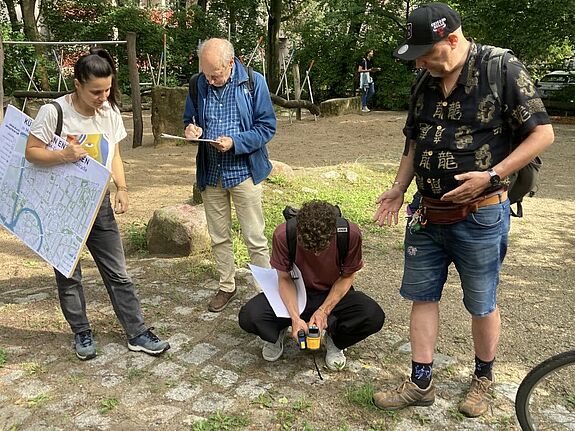 Vier Personen untersuchen im Freien mit Messgerät und Stadtplan die Temperatur am Boden.