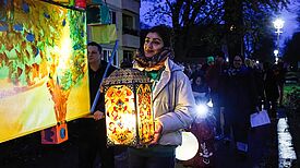 Eine Frau trägt eine leuchtende, kunstvoll verzierte Laterne beim Laternenumzug des Lichtermarkts.