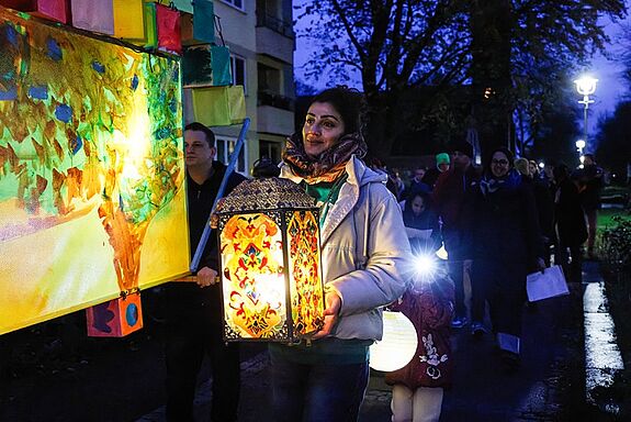 Eine Frau trägt eine leuchtende, kunstvoll verzierte Laterne beim Laternenumzug des Lichtermarkts.