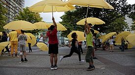 Die Bewohnerinnen und Bewohner des Kiezes haben sich zusammen mit gelben Schirmen in große Skulpturen verwandelt. (Foto: Rosa Vill)