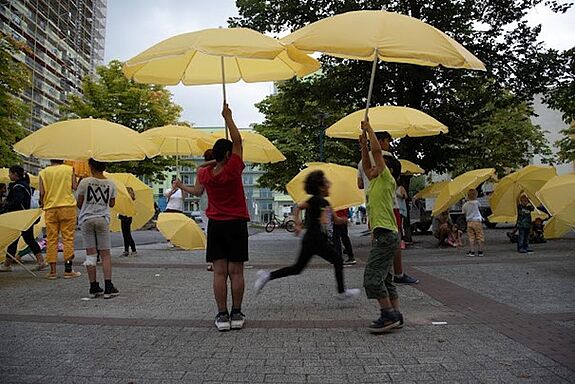 Die Bewohnerinnen und Bewohner des Kiezes haben sich zusammen mit gelben Schirmen in große Skulpturen verwandelt. (Foto: Rosa Vill)