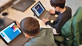 Zwei Jungs in einem Klassenzimmer sitzen an zwei iPads.