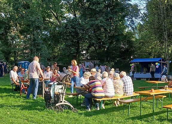 Menschen sitzen an Bierzeltgarnituren auf einer Wiese im Volkspark Lichtenrade, unterhalten sich und genießen das sonnige Wetter beim Erntedankfest.