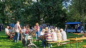 Menschen sitzen an Bierzeltgarnituren auf einer Wiese im Volkspark Lichtenrade, unterhalten sich und genießen das sonnige Wetter beim Erntedankfest.