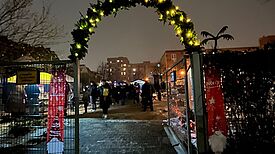 Hinter einen mit Licht geschmückten Tor befindet sich ein Wintermarkt. 