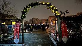 Hinter einen mit Licht geschmückten Tor befindet sich ein Wintermarkt. 