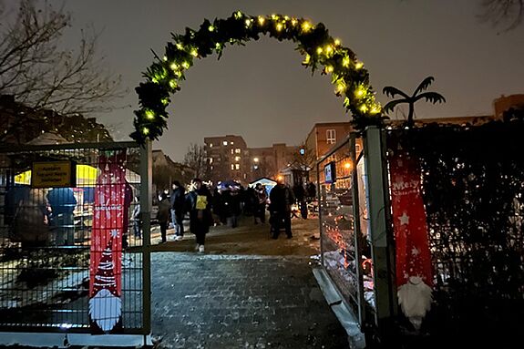 Hinter einen mit Licht geschmückten Tor befindet sich ein Wintermarkt. 