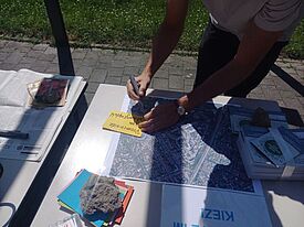 Ein Tisch im Außenraum mit bunten Zetteln und einem Plan. Eine Person schreibt Notizen auf einen gelben Zettel.