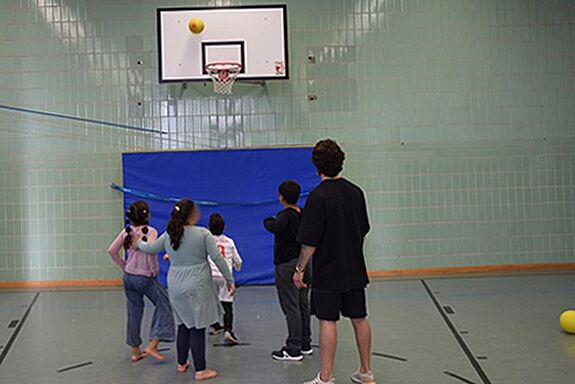 Gemeinsam mit einem Trainer werfen Kinder Bälle in einen Basketball-Korb.