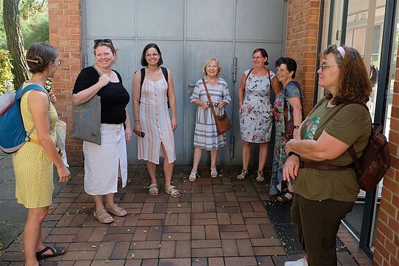 Sieben Teilnehmerinnen des Ausflugs stehen beim Besuch des Baudenkmals „Mies van der Rohe Haus“ in einer Gruppe zusammen. 