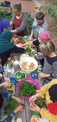 Mehrere Personen sind um einen Tisch versammelt, an dem sie gemeinsam kochen. 