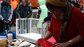 Künstlerin in rotem Pullover repariert beim BSR-Kieztag im Harzer Kiez ein Möbelstück, umgeben von Besucherinnen und Besuchern.