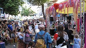 Viele Menschen stehen und sitzen vor einer Bühne beim Kiezfest in der Weichselstraße im QM-Gebiet Donaustraße-Nord.