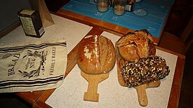 Verschiedene frisch gebackene Brote liegen auf Holzbrettern auf einem Tisch.  