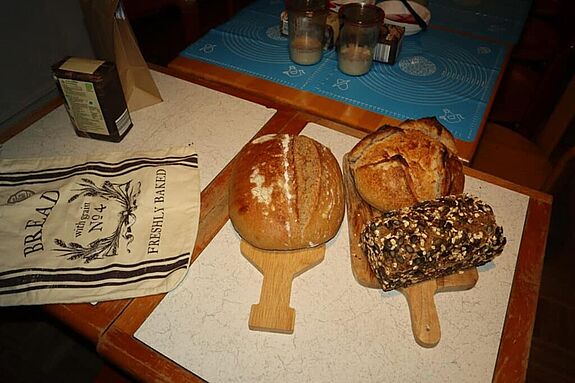 Verschiedene frisch gebackene Brote liegen auf Holzbrettern auf einem Tisch.  