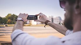 Person fotografiert mit dem Smartphone eine Straßenszene.