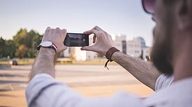 Person fotografiert mit dem Smartphone eine Straßenszene.