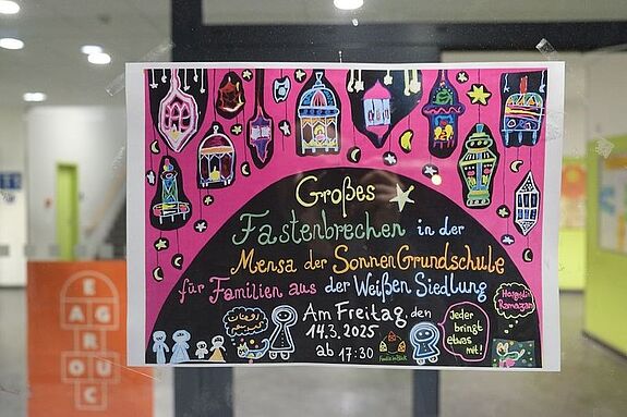Auf einem bunten Plakat steht der Einladungstext zum Fastenbrechen im QM-Gebiet Dammwegsiedlung / Weiße Siedlung. 
