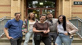 Fünf Projektbeteiligte des Bildungsprojekts „Außerschulische Lernorte“ stehen vor einem Gebäude der Herbert-Hoover-Schule im Berliner Quartier Reinickendorfer Straße /Pankstraße.