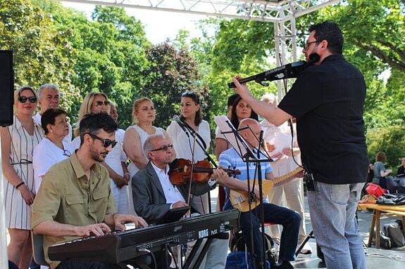 Eine Musikgruppe mit Chor, Keyboarder, Violinist und Gitarrist tritt auf einer Bühne im Freien vor Publikum beim Sommerfest im QM-Gebiet Brunnenstraße auf.